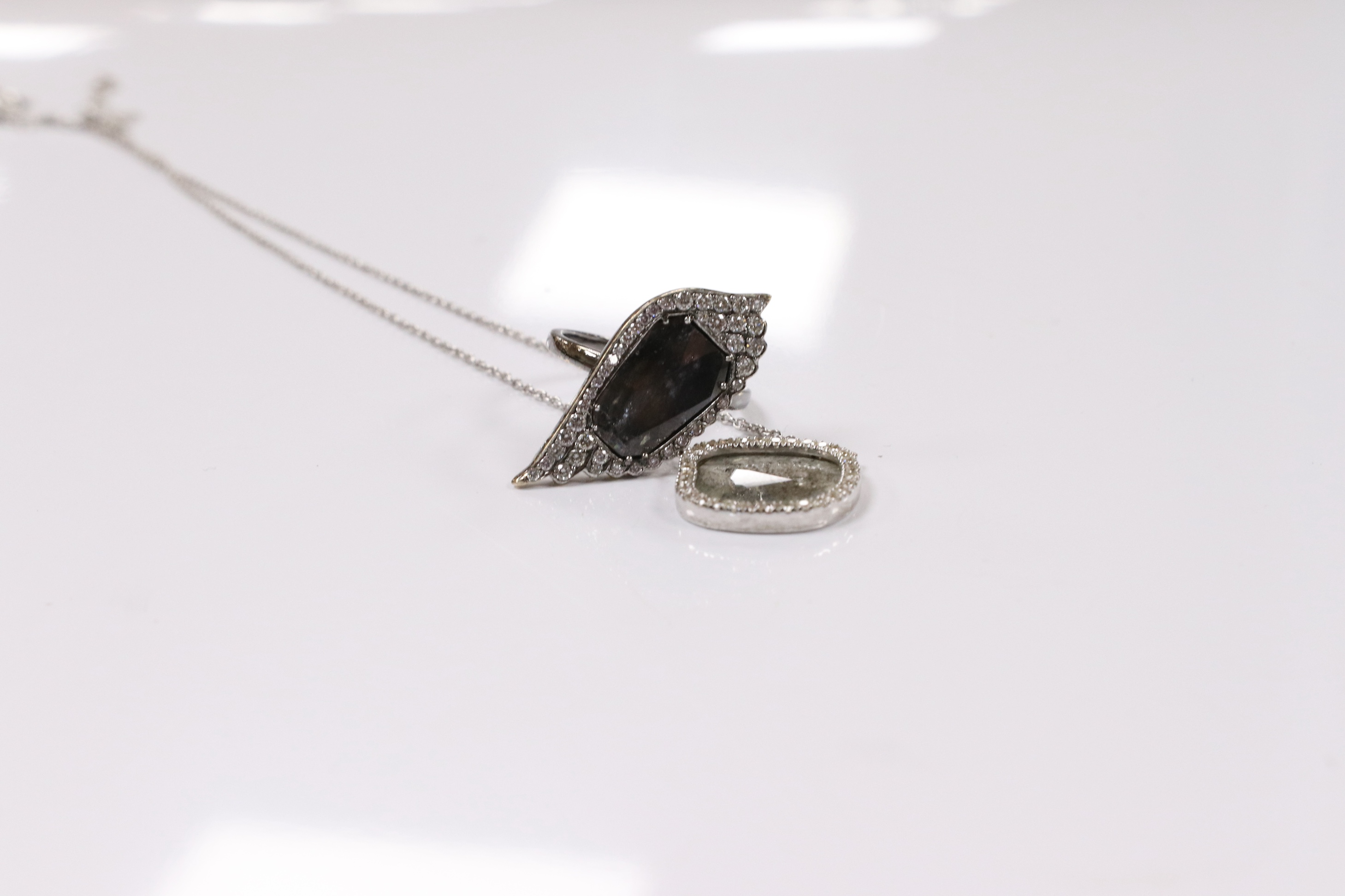 A modern suite of 18k and diamond set jewellery by Pebble, comprising a dress ring and pendant necklace, each with a slither of diamond bordered by brilliants, ring size M, pendant necklace overall 46cm, gross weight 11.